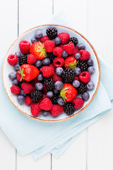 Fresh berry salad on blue dishes. Vintage wooden background.