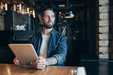 Modern hipster businessman drinking coffee in the city cafe during lunch time and working on tablet