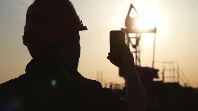 Engineer worker on an oil rig take photo with smartphone. Oil industry using mobile phone communication.