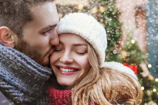 Young man kissing happy smiling woman on cheek. Cute young couple  posing in street. Christmas background