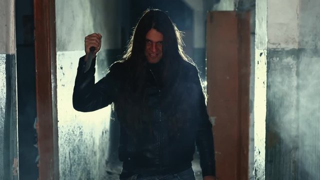 Crazy criminal or maniac with knife in hand in old scary building looks at camera, serial killer with cold weapon