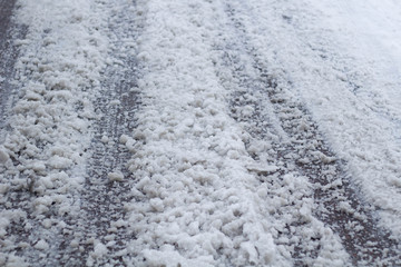 Winter puddles and snow slush on road with traces of tires during the thaw