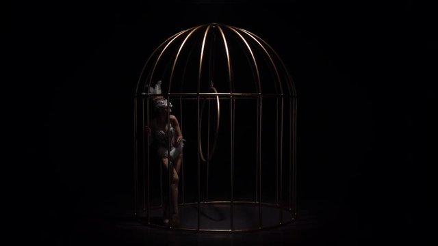 Acrobatics aerial on a rotating hoop in a cage room. Black background. Slow motion