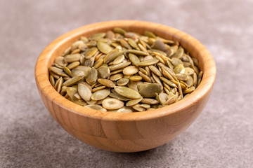Fresh pumpkin seeds in wooden bowl on marble background