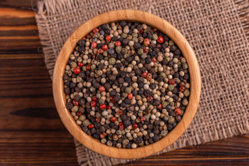 Mix of peppers in bowl burlap napkin on wooden background