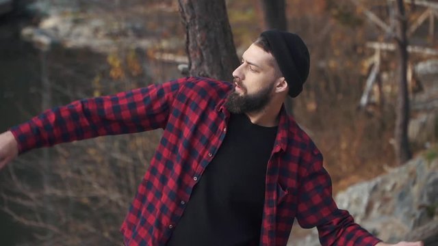 Young bearded guy throws stone in the water. Brutal man with a black beard wolks outdoors.
