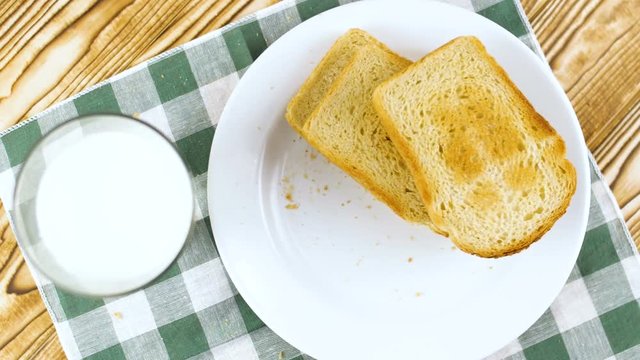 Toast bread falling on white plate with milk in glass on wooden kitchen surface. Slow motion footage.
