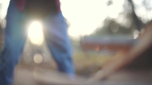 A man in plaid shirt and jeans chops wood in two pieces. Forester cuts wood.