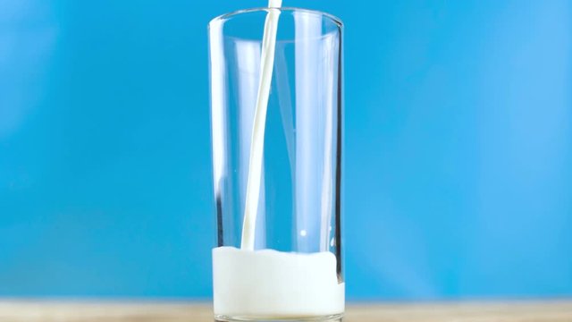 White milk pouring intro glass on blue background. Slow motion footage.