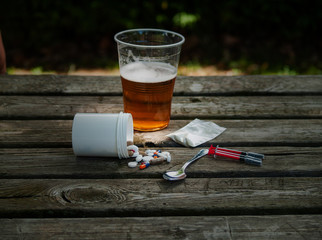 A glass of beer, pills, barbiturates, drugs, cocaine, heroin, a syringe and a spoon on a table. Drug addiction concept