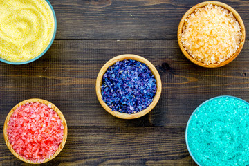 Spa salt background. Colorful spa salt in bowls on dark wooden background top view. Yellow, turquoise, pink, purple spa salt