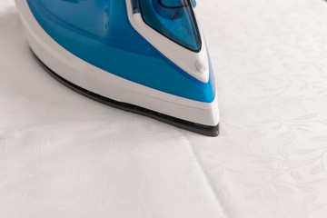 An iron standing on ironing board on white tablecloth