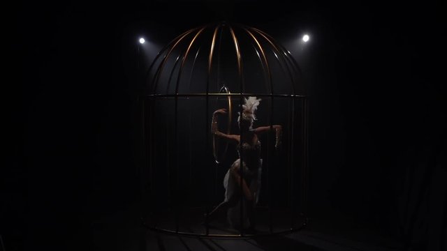 Graceful girl gymnast riding a hoop in a cage on dark stage. Black background. Slow motion