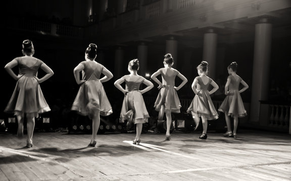 blurred silhouettes of girls in ball gowns dancing on stage in the theater in front of the audience during a concert.