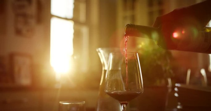 Man Pouring Red Wine Into Glass At Kitchen Table