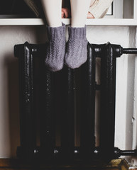 A girl sits on a windowsill put their feet in knitted woolen socks on the radiator and heated on a...