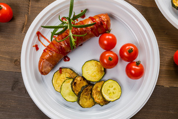 Plate with grilled sausage, cucumber and tomatoes on the wooden table