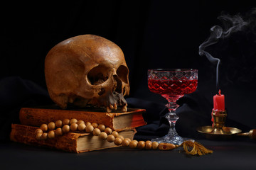 A skull, a rosary, a glass of wine and an unlit candle