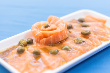 White plate with salmon sashimi, capers and shoyu