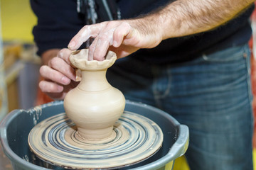 Potter's hands close-up with pot and pottery wheel.