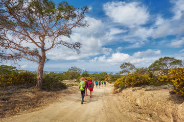 group of tourists with large backpacks are on the sandy road to the sea