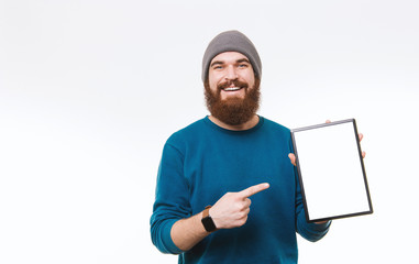 Studio shot of happy bearded hipster man pointing at blank screen on tablet