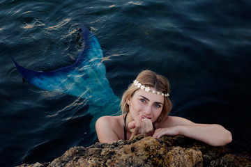 mermaid swims in the water peeking out of the rocks.