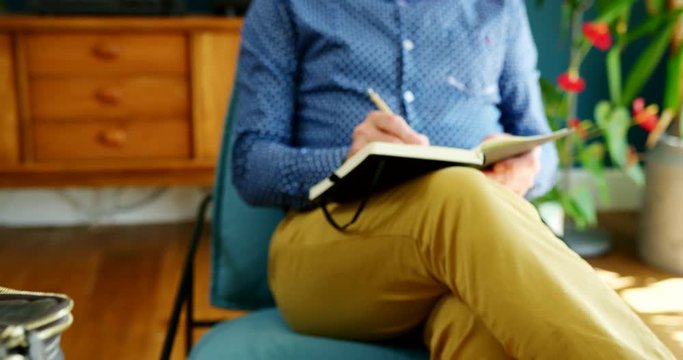 Casual Businessman Sitting On Chair And Writing Notes In A Journal
