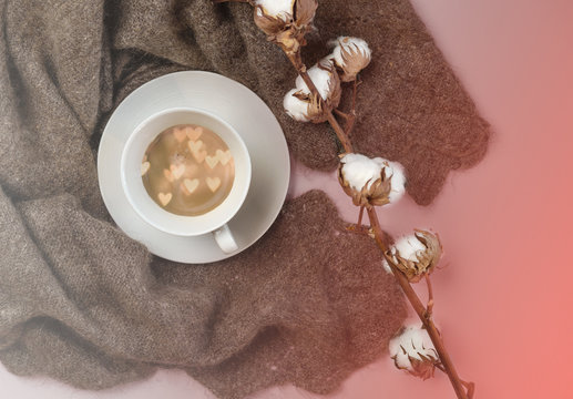 Flat lay Russian woolen shawl with cup of coffee with hearts inside and cotton branch on color of the year 2019 Living Coral background. toned. Top view. Valentines day winter layout. for blogger.