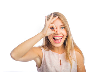 Young beautiful blonde woman shows okay near her eyes and smiles enthusiastically with her mouth open, close-up shot on an isolated background