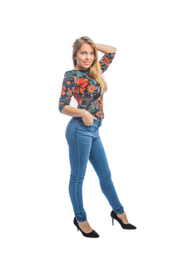 Beautiful young woman with long blond hair in jeans, a blouse and shoes posing with one hand on her head and the other hand in a jeans pocket, profile photo.