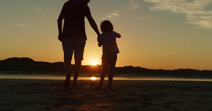 Silhouette Of Father And Son Walking Together At Beach