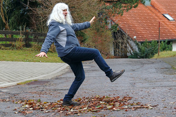 Gefahr im Herbst. Eine Frau rutscht auf einer Straße auf nassem Laub aus. 