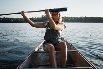 Portrait of happy woman with mouth open holding oar while sitting in boat on river against sky