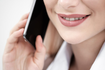 Close-up of the mouth and lips of a woman talking on a smartphone on a white background.