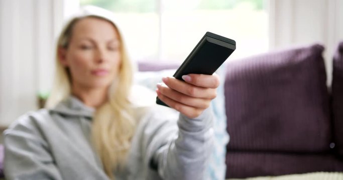 Beautiful Blond Woman Using TV Remote Control Sitting On Sofa