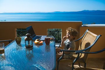 Funny child smile. Laughing child in morning terrace near sea. The best family vacation. Tourism and pleasure life. Healthy breakfast. Fruit and morning coffee. Beautiful weather for summer holidays