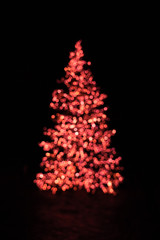 Blurry Christmas tree illuminated with red and orange fairy chain lights at night during advent seasin creating beautiful bokeh effect with glowing circles