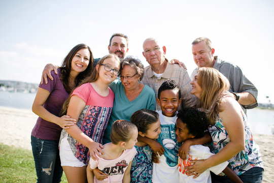 Happy multi-generation family standing at beach against sky during sunny day