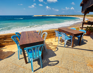 Tables and chairs in a cafe with palm trees on the beach Lara