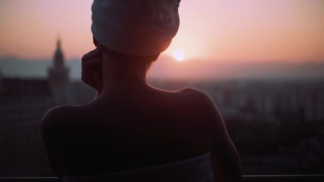 Young silhouette woman with a wrapped towel on his head look around on balcony at sunset amazing view relaxed day female morning sunny girl bath attractive alone city enjoying slow motion
