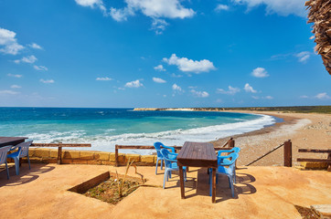 Tables and chairs in a cafe with palm trees on the beach Lara