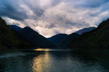 Lake in the mountains. Sunset with reflection in the water. Thunderclouds in the sky. Evening landscape. Twilight on the lake.