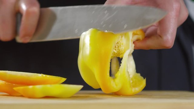 Close up shot of hands of unrecognizable male cook cutting yellow bell pepper on wooden board