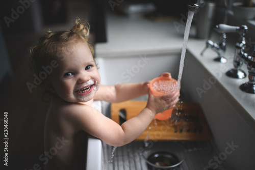 Portrait of smiling shirtless girl with messy mouth filling water in glass