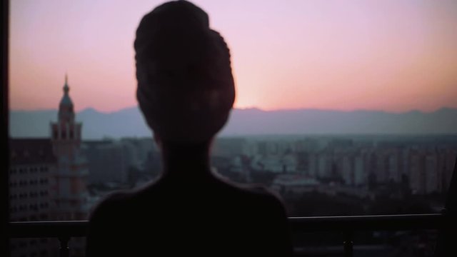 Amazing view young silhouette woman with a wrapped towel on his head on balcony at sunset looking at the city relaxed day female morning sunny girl bath attractive alone city enjoying slow motion