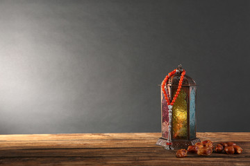 Muslim lamp, dates and prayer beads on wooden table against dark background. Space for text