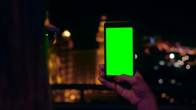 Close up woman hand holding phone with green screen blurred night city light vertical display touchscreen online internet concept communication application