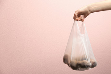 Woman holding plastic bag with potatoes on color background, closeup. Space for text