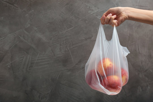 Woman holding plastic bag with apples on gray background. Closeup, space for text